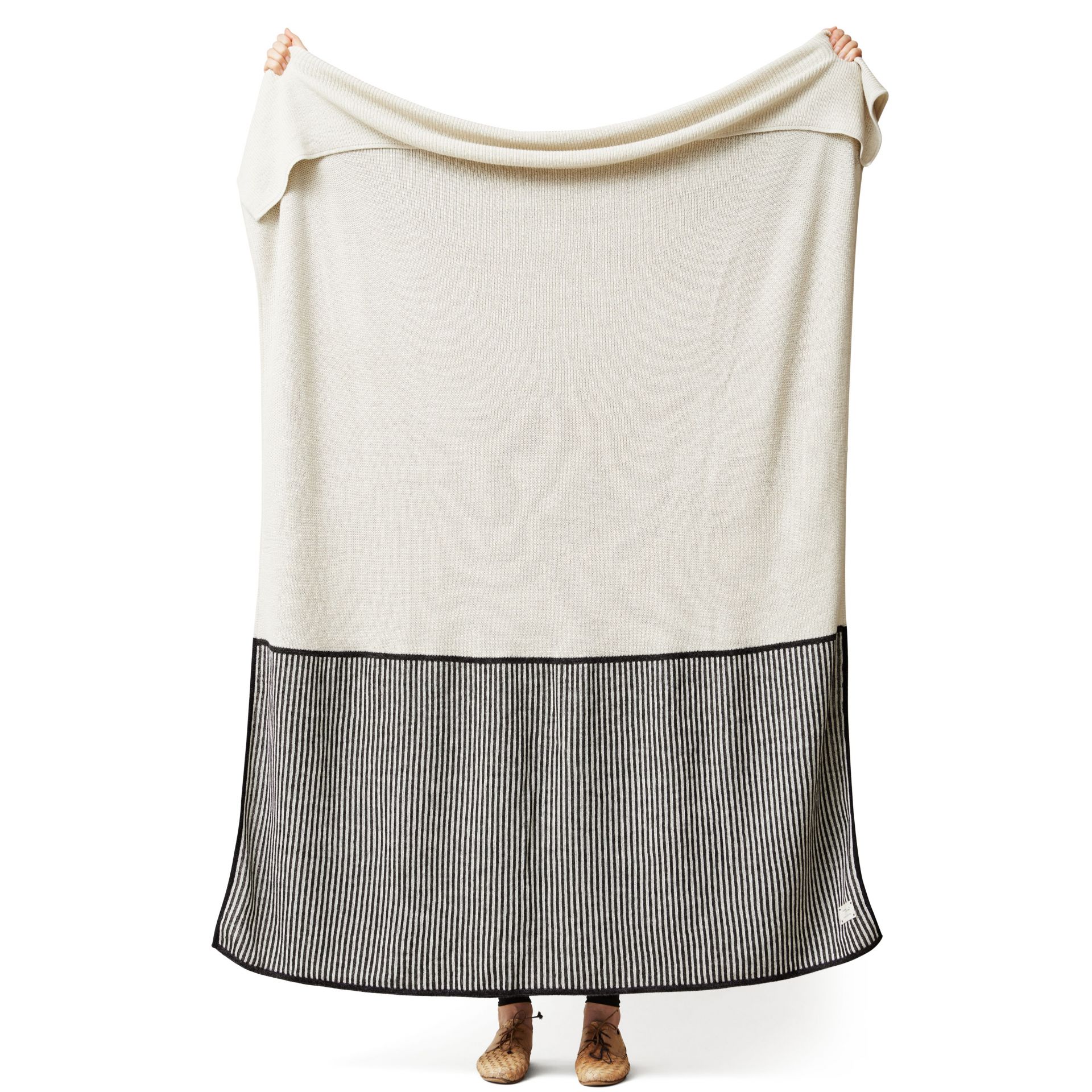 Aymara Decke in Creme mit schwarzen Streifen, gehalten von zwei Händen. Kuscheldecke für Zuhause.